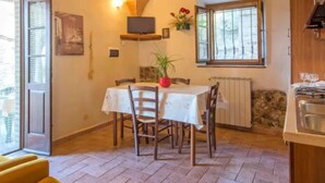 Un comedor acogedor con una mesa preparada para cuatro personas, un televisor sobre la mesa y una ventana con vistas al exterior.