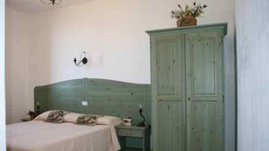 Quarto com cama, mesa de cabeceira, luminária na parede e guarda-roupa verde.