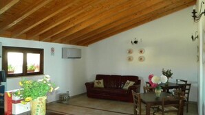 Uma sala de estar aconchegante com teto de madeira, um sofá vermelho, uma mesa de jantar com cadeiras e uma área de cozinha com fogão e armários.