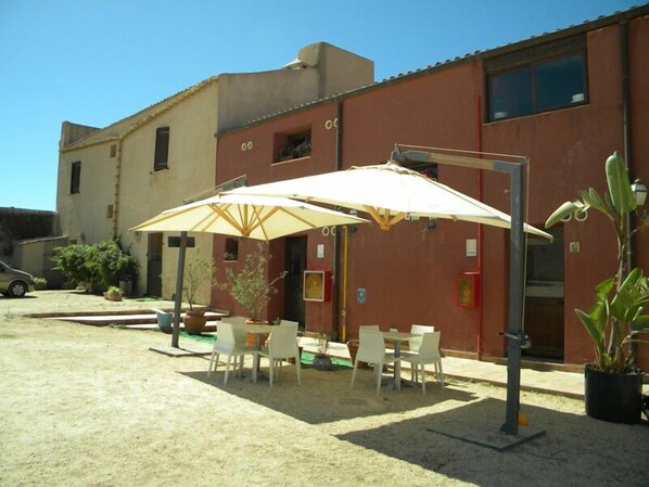 An outdoor seating area with tables and chairs under umbrellas, a building with a red facade, and a parked car.