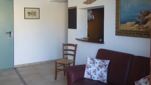 Uma sala de estar com um sofá vermelho, uma cadeira de madeira, um lustre, um quadro emoldurado e uma porta.