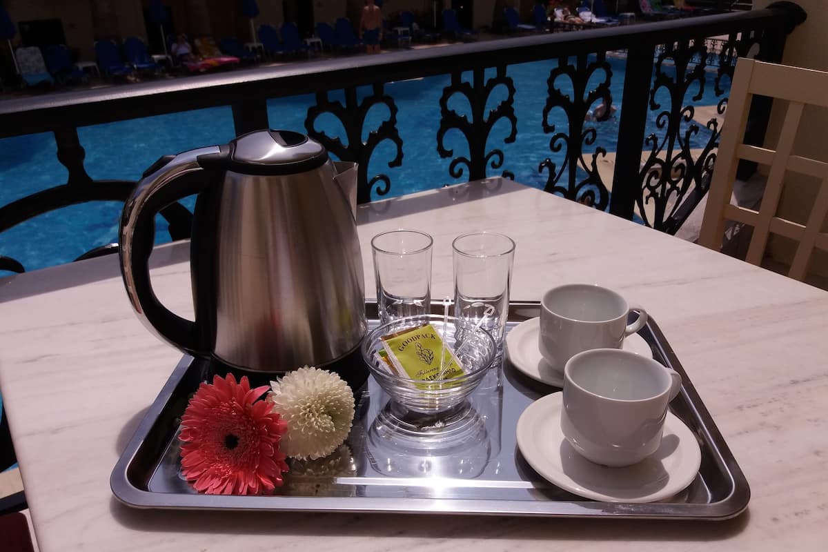 Un plateau avec une théière, des tasses à thé, des verres et des fleurs, posé sur une table près d’une piscine.