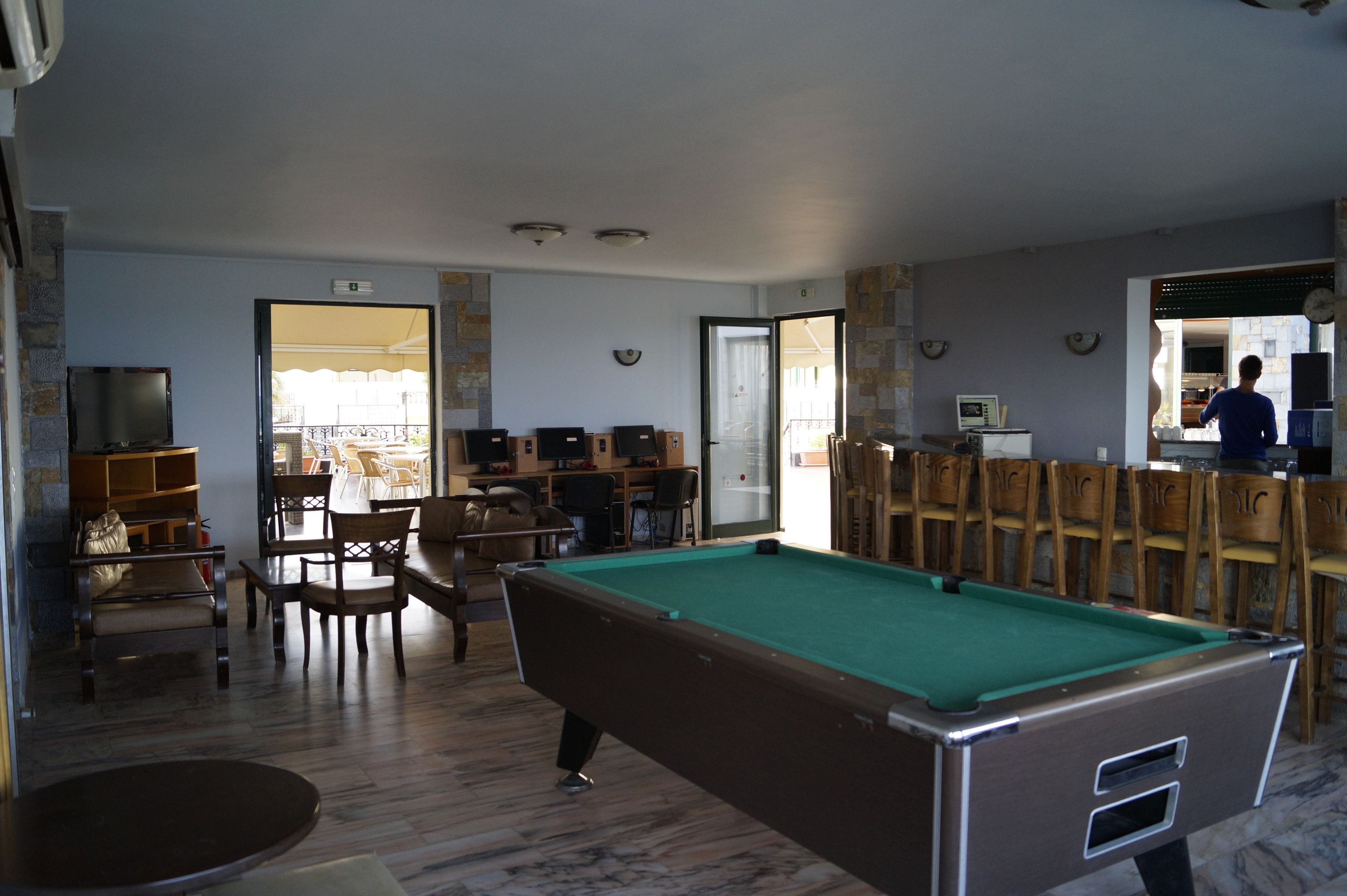 A pool table in a room with a wooden chair arrangement, a television, and a door leading outside.