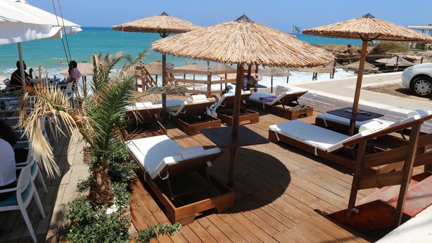 Une terrasse en bois avec des chaises longues et des parasols en chaume, offrant une vue sur la mer.