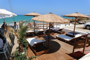 Terraza de madera con tumbonas y sombrillas de paja con vista al mar.