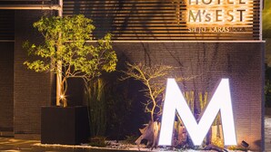 On peut voir une enseigne d’hôtel avec les inscriptions « HOTEL M’s EST » et « SHIJO KARASUMA ».