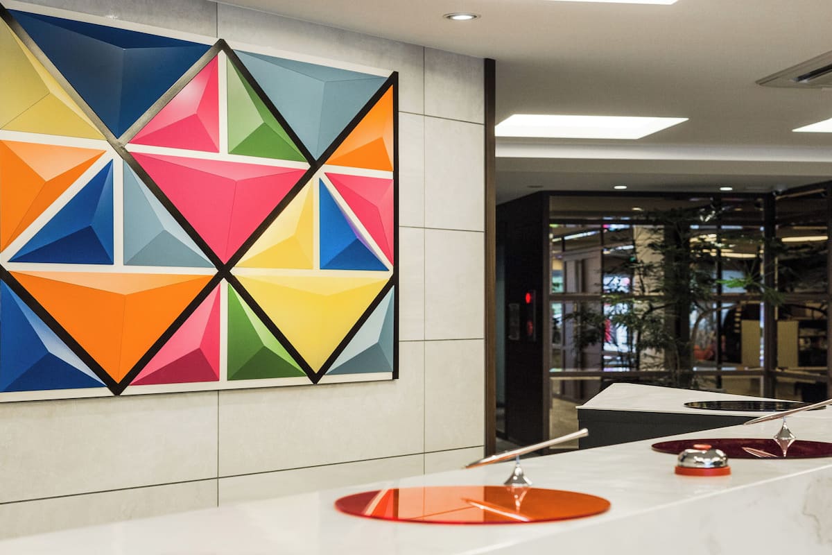 Un hall d’hôtel moderne, orné d’une œuvre d’art géométrique au mur, avec un comptoir d’accueil et une porte en verre donnant sur l’intérieur.