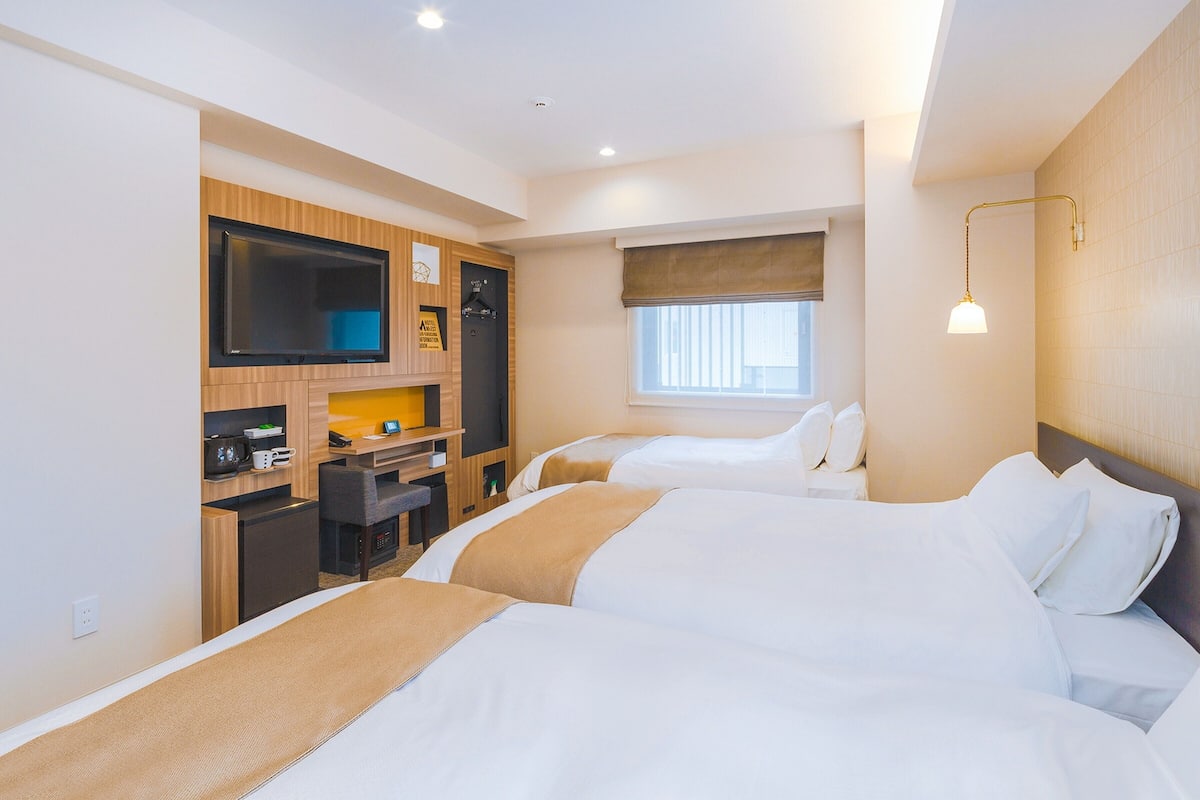 Une chambre d’hôtel avec deux lits, un bureau avec une télévision et une fenêtre avec des stores.