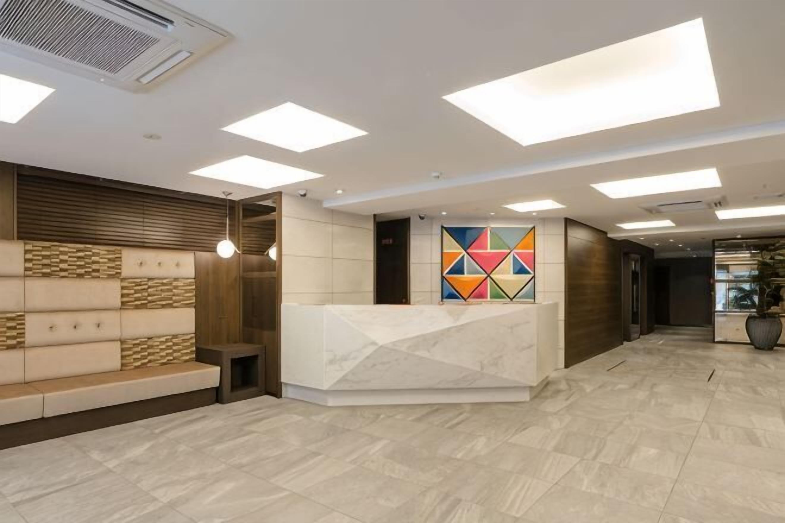 A reception area with a marble counter, a geometric wall art, a seating area with patterned cushions, and a tiled floor.