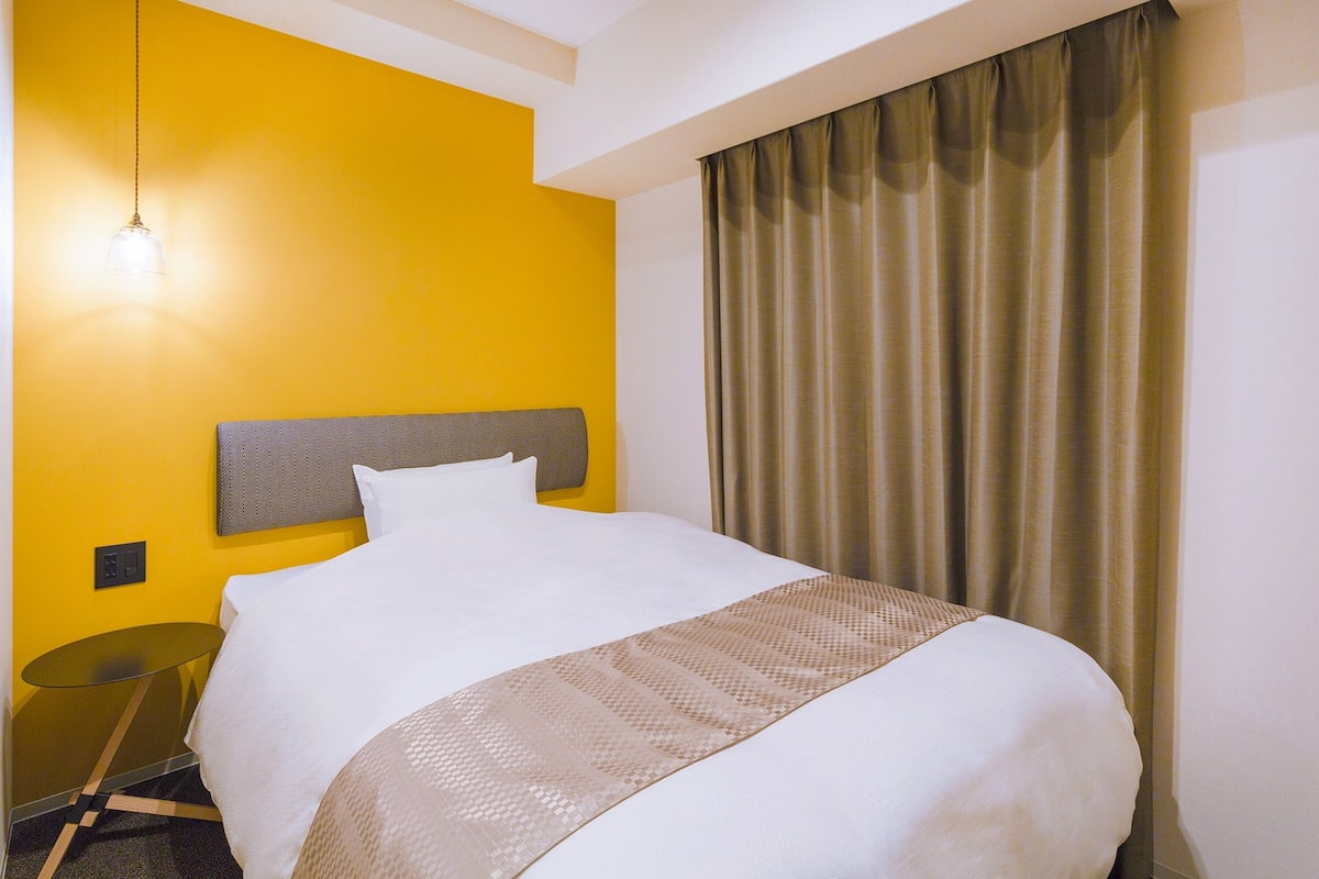 Une chambre d’hôtel avec un grand lit, une table de chevet, une lampe et une fenêtre avec des rideaux.