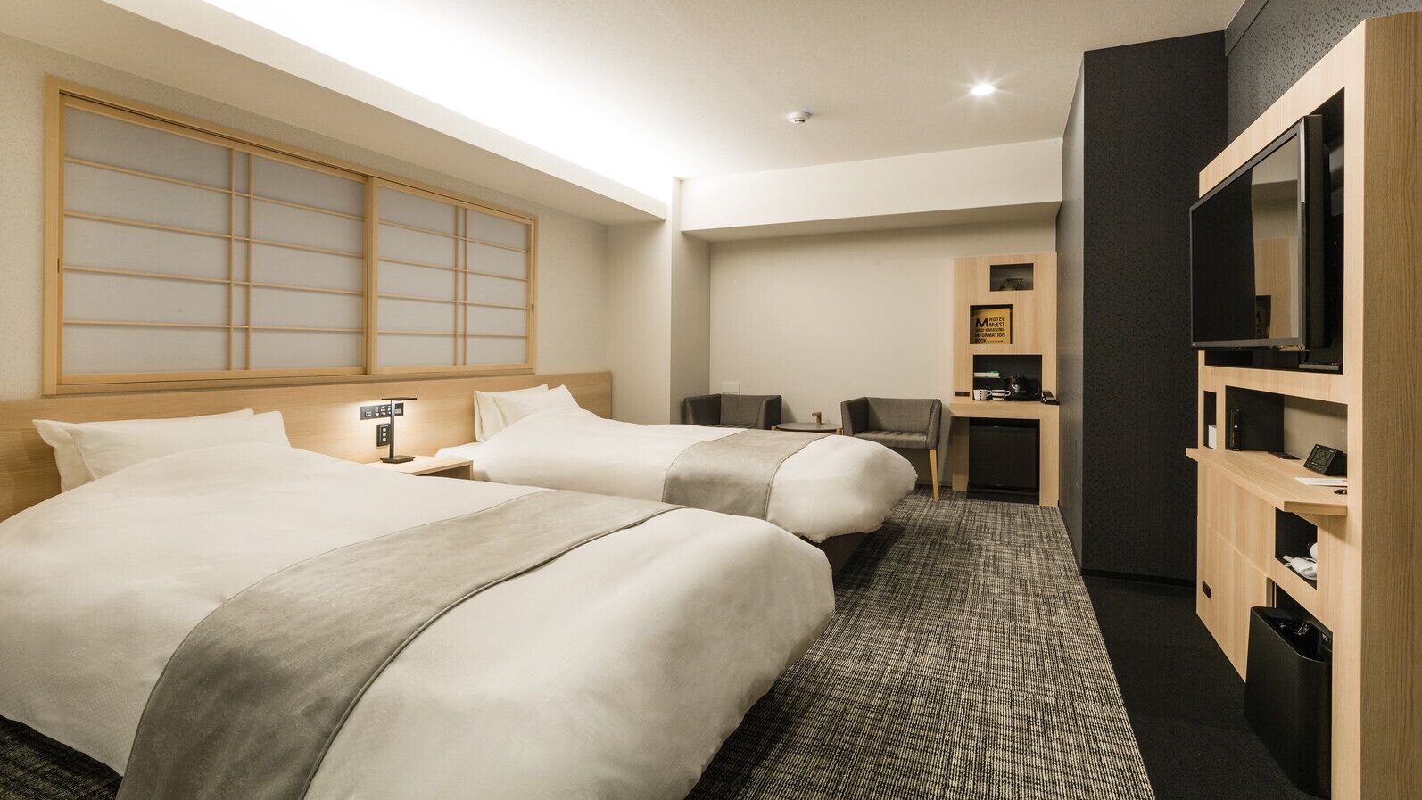 Habitación de hotel con dos camas, un escritorio, una silla, televisión y minibar.