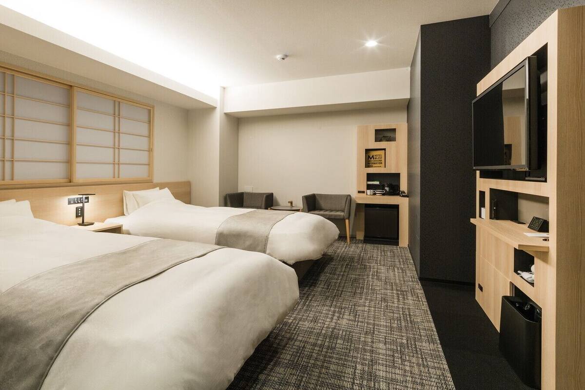 Une chambre d’hôtel avec deux lits, un bureau, une chaise, une télévision et un mini-bar.