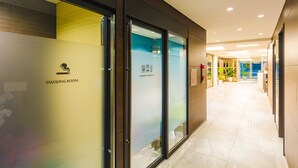 Un couloir avec une porte indiquant l’emplacement d’une salle fumeurs, une porte vitrée et un panneau indiquant l’emplacement d’une laverie en libre-service.