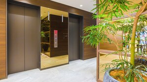 Un ascenseur moderne doté d’une porte en verre, d’un mur en bois et d’une plante en pot placée à côté.