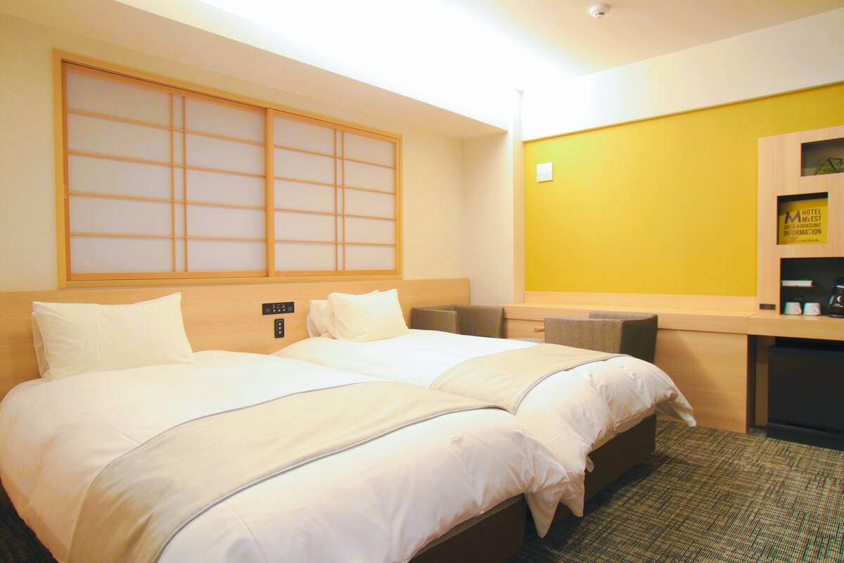 Une chambre d’hôtel avec deux lits, une tête de lit en bois, un mur d’accent jaune et un petit bureau avec un miroir.