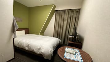 Una habitación de hotel con una cama, una mesita de noche con un control remoto, una pequeña mesa redonda con un folleto y una ventana con cortinas.