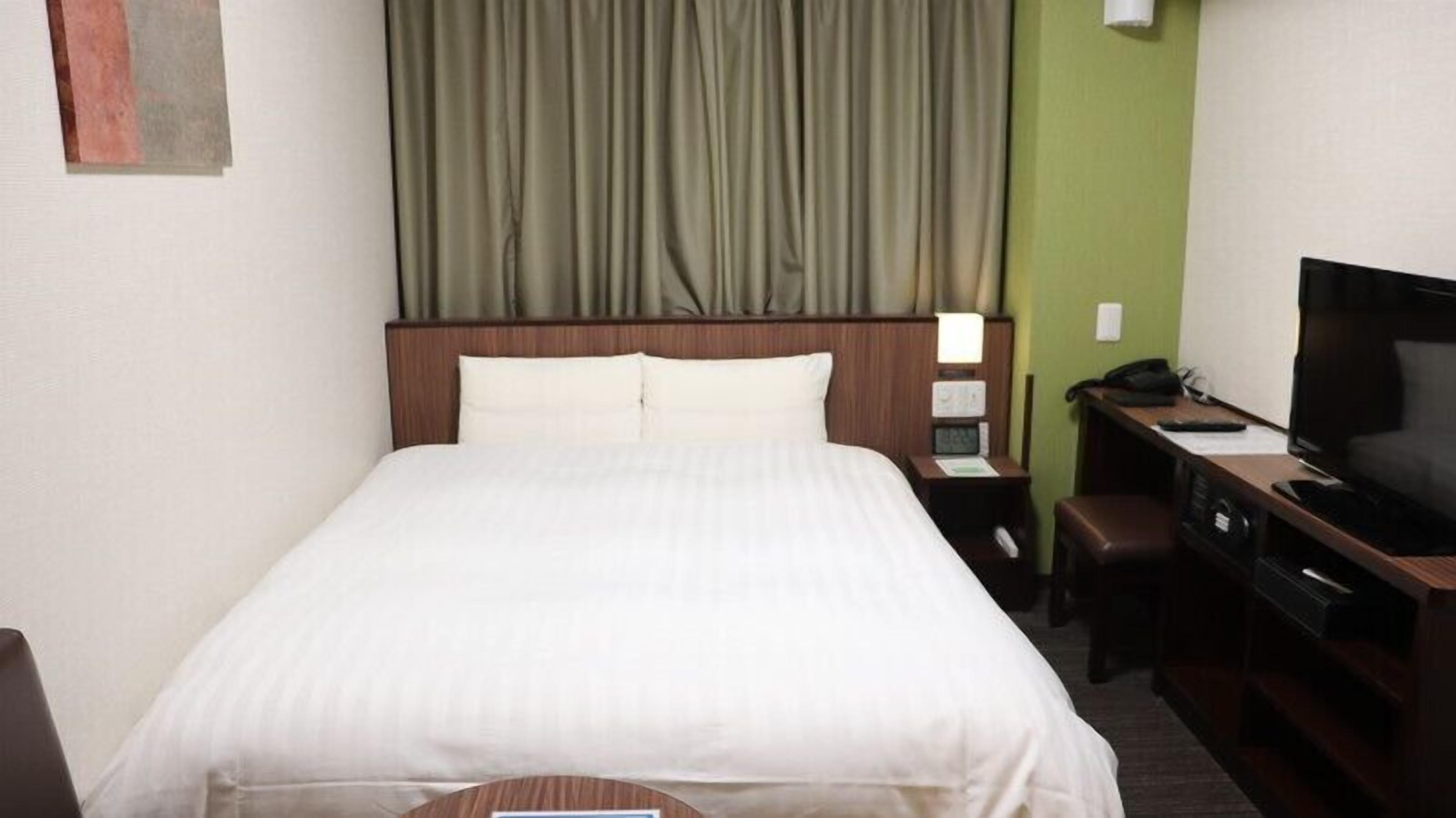 Una habitación de hotel con cama, escritorio con computadora, televisor y mesita de noche.