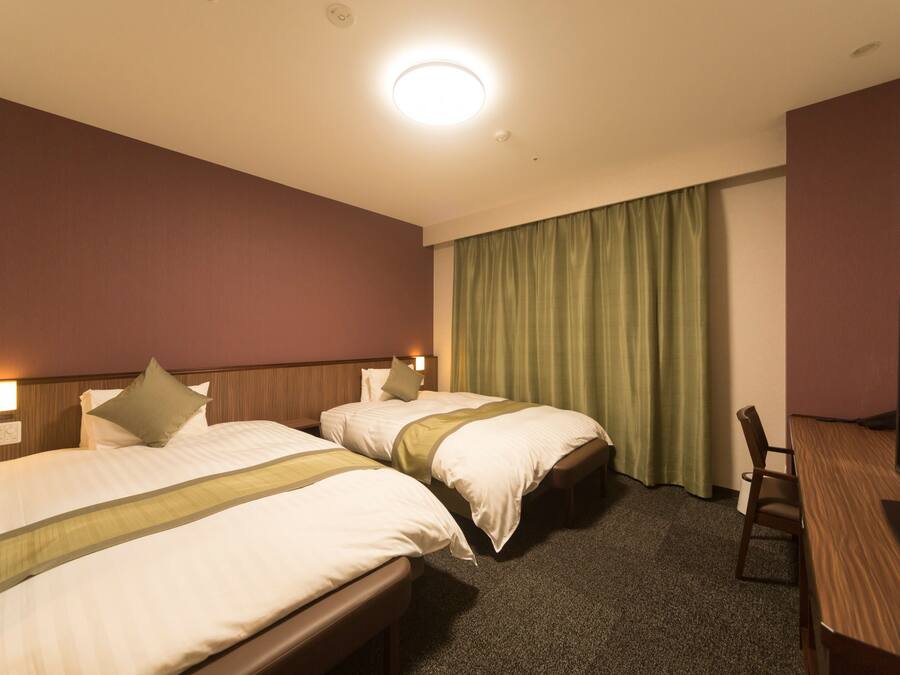 Habitación de hotel con dos camas, un escritorio y una televisión.