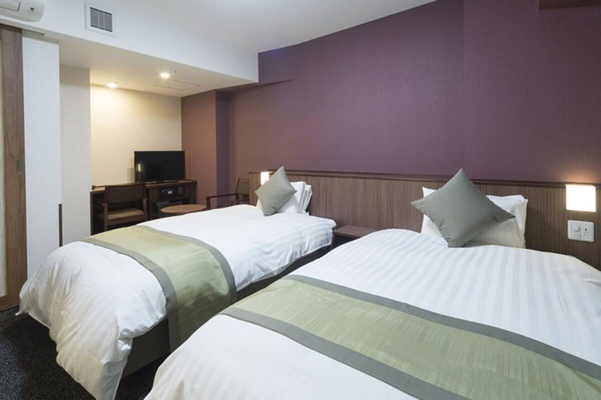 A hotel room with two beds, a television, and a desk.
