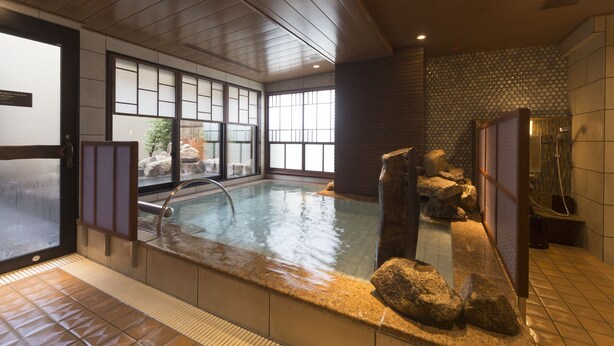 Un onsen japonés tradicional con interior de madera, una fuente termal de piedra y vistas al exterior a través de amplios ventanales.