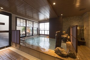 Een traditionele Japanse onsen met een houten inrichting, een stenen warmwaterbron en uitzicht op de natuur door grote ramen.