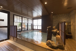 Un onsen japonés tradicional con interior de madera, una fuente termal de piedra y vistas al exterior a través de amplios ventanales.
