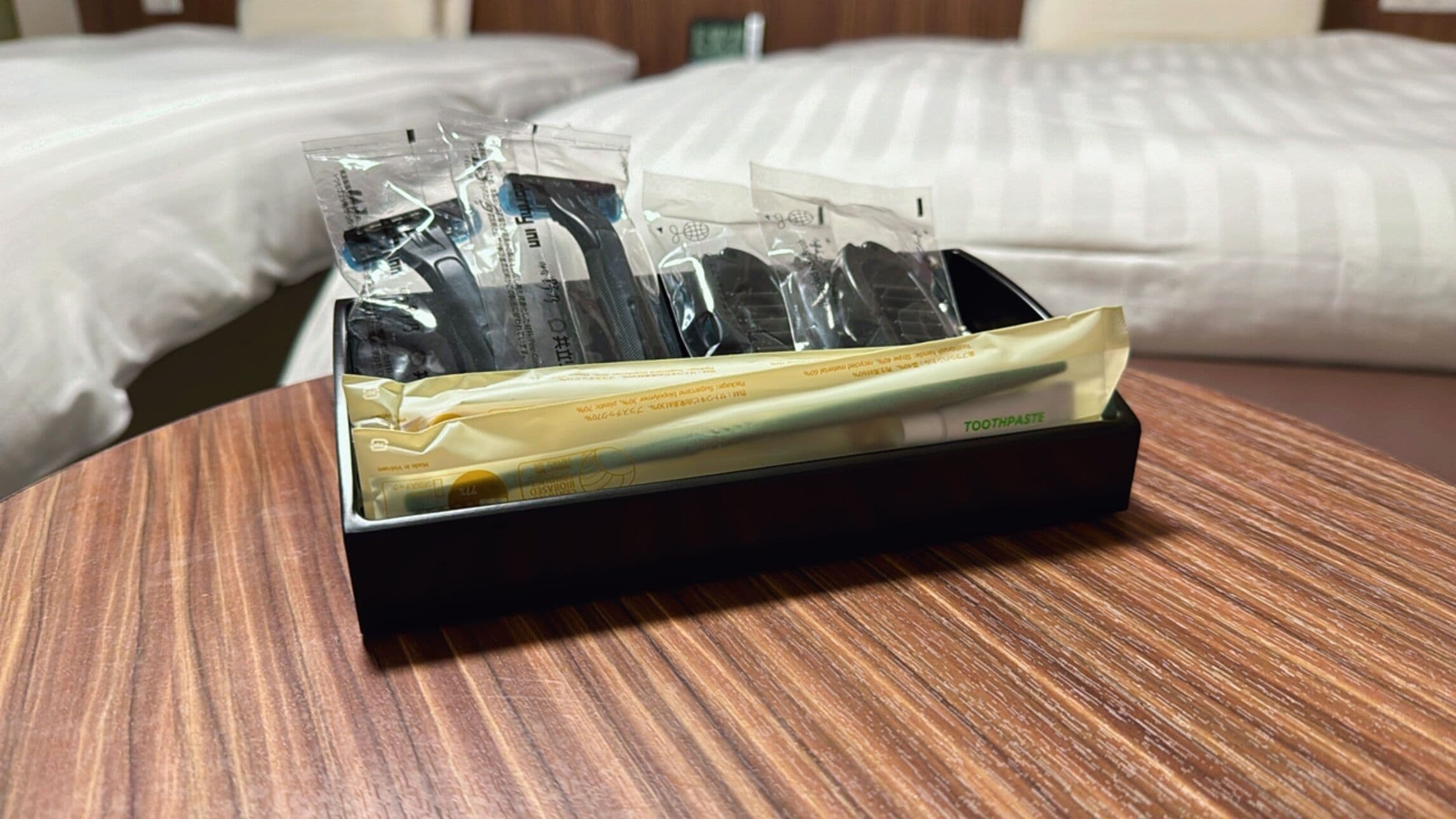 Un plateau noir contenant plusieurs brosses à dents et un tube de dentifrice, posé sur une table en bois dans une chambre d’hôtel.