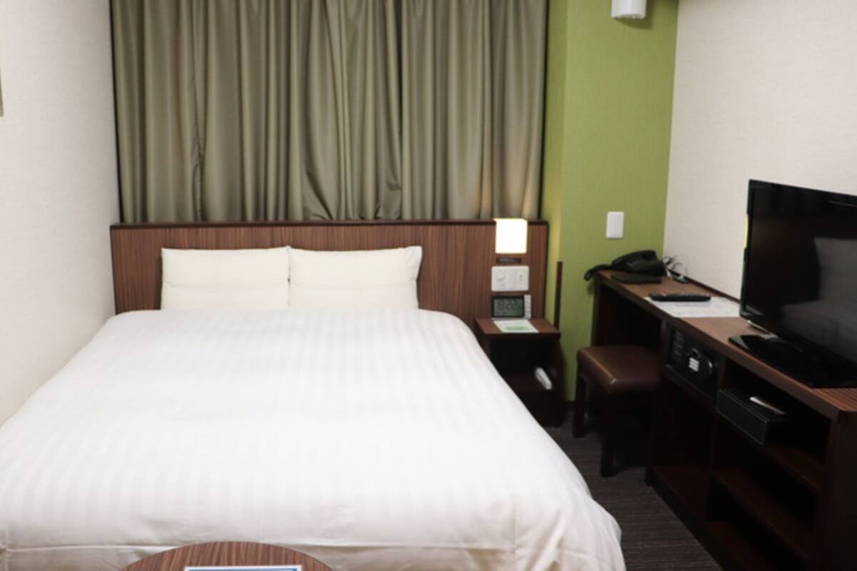 A hotel room with a large bed, a desk with a computer and a TV, and a green wall.