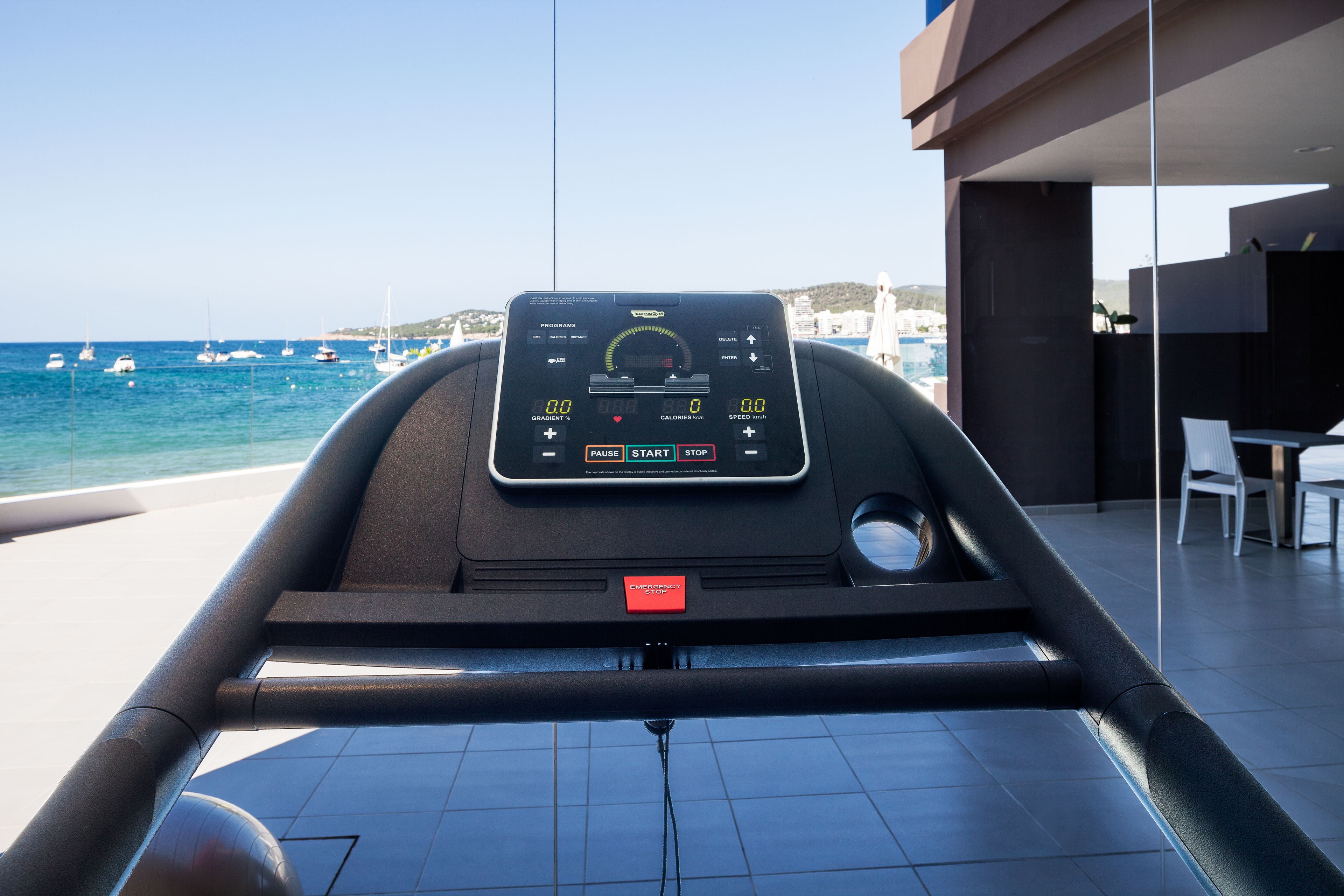 A treadmill with a digital display, a control panel, and a red emergency stop button.