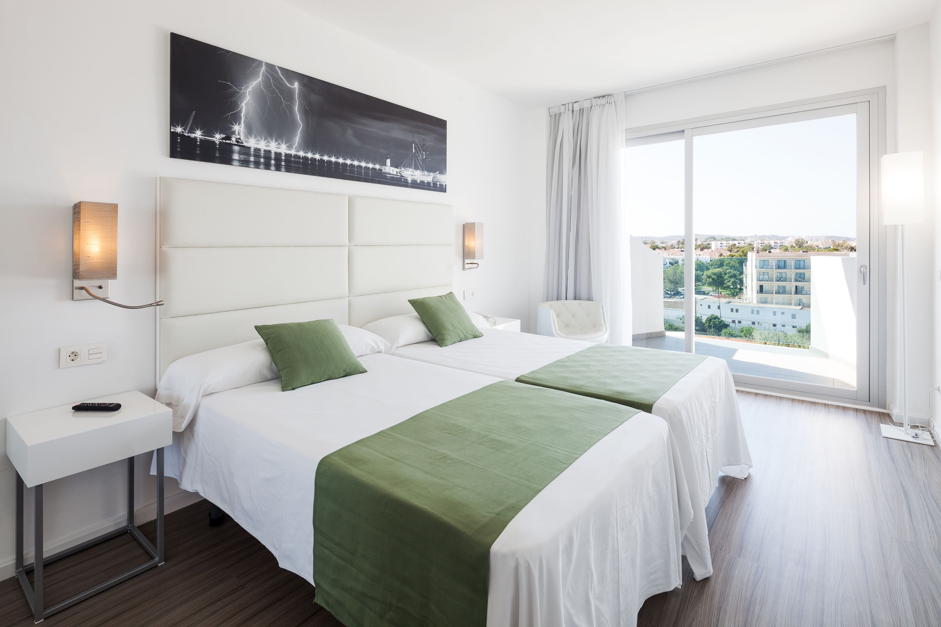A hotel room with two beds, a large window with a view, and a painting on the wall.