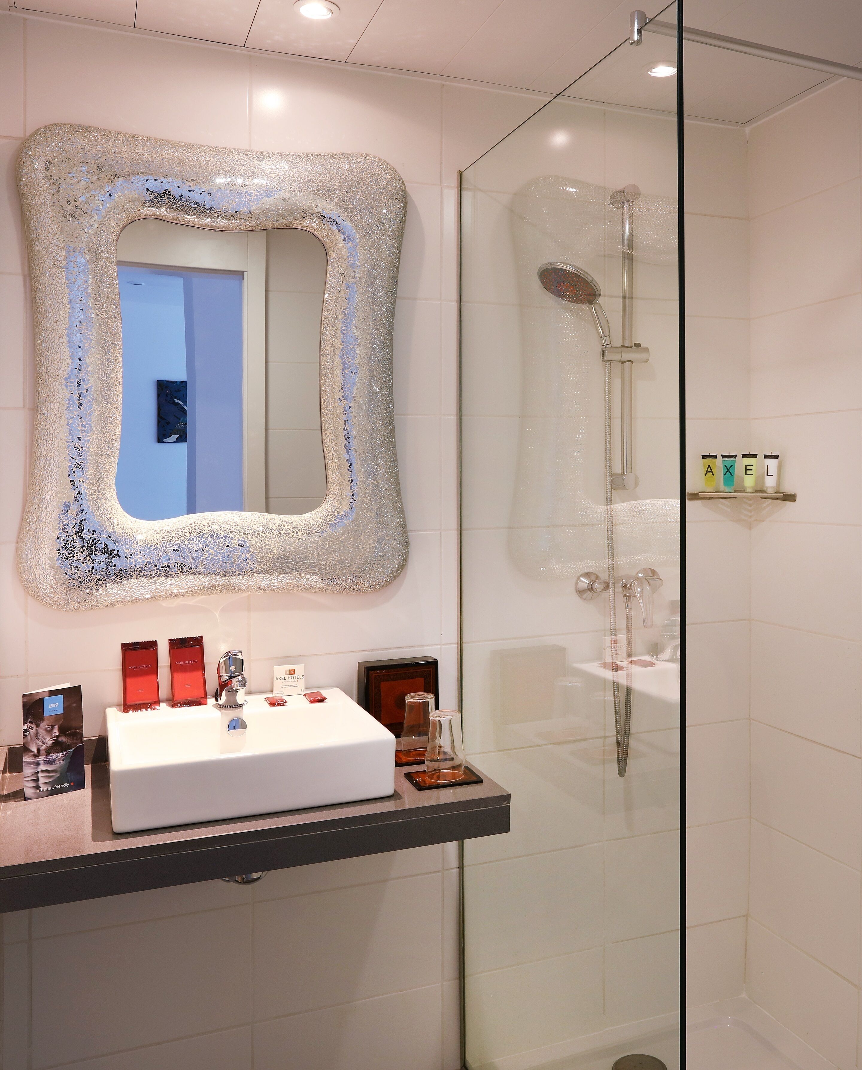Une salle de bain moderne avec un grand miroir, une douche et un meuble-lavabo avec des articles de toilette.