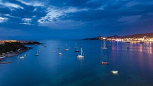 A coastal marina with multiple boats anchored in calm waters, a distant cityscape with illuminated buildings, and a clear sky. - Axel Beach Ibiza - Adults Only (Sant Josep de sa Talaia)
