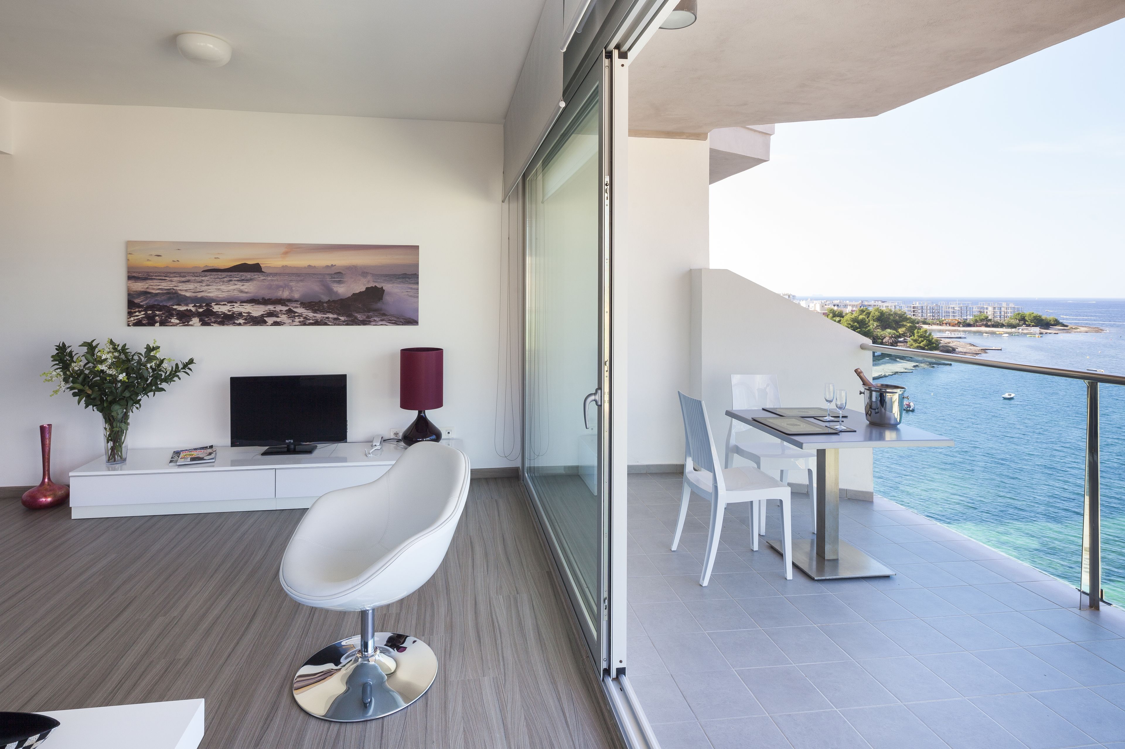Un balcon moderne doté d’un espace repas, d’un téléviseur et d’un tableau représentant un paysage côtier.