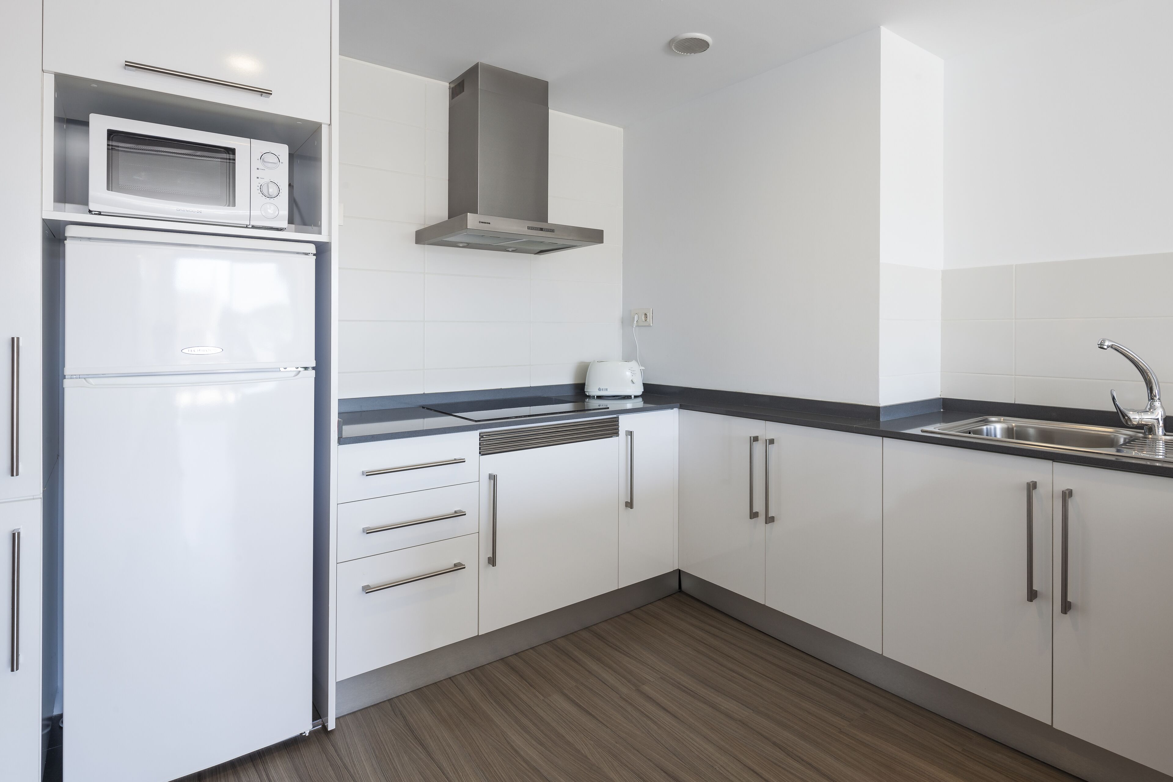 Una cocina moderna con armarios blancos, microondas integrado y pileta de acero inoxidable.