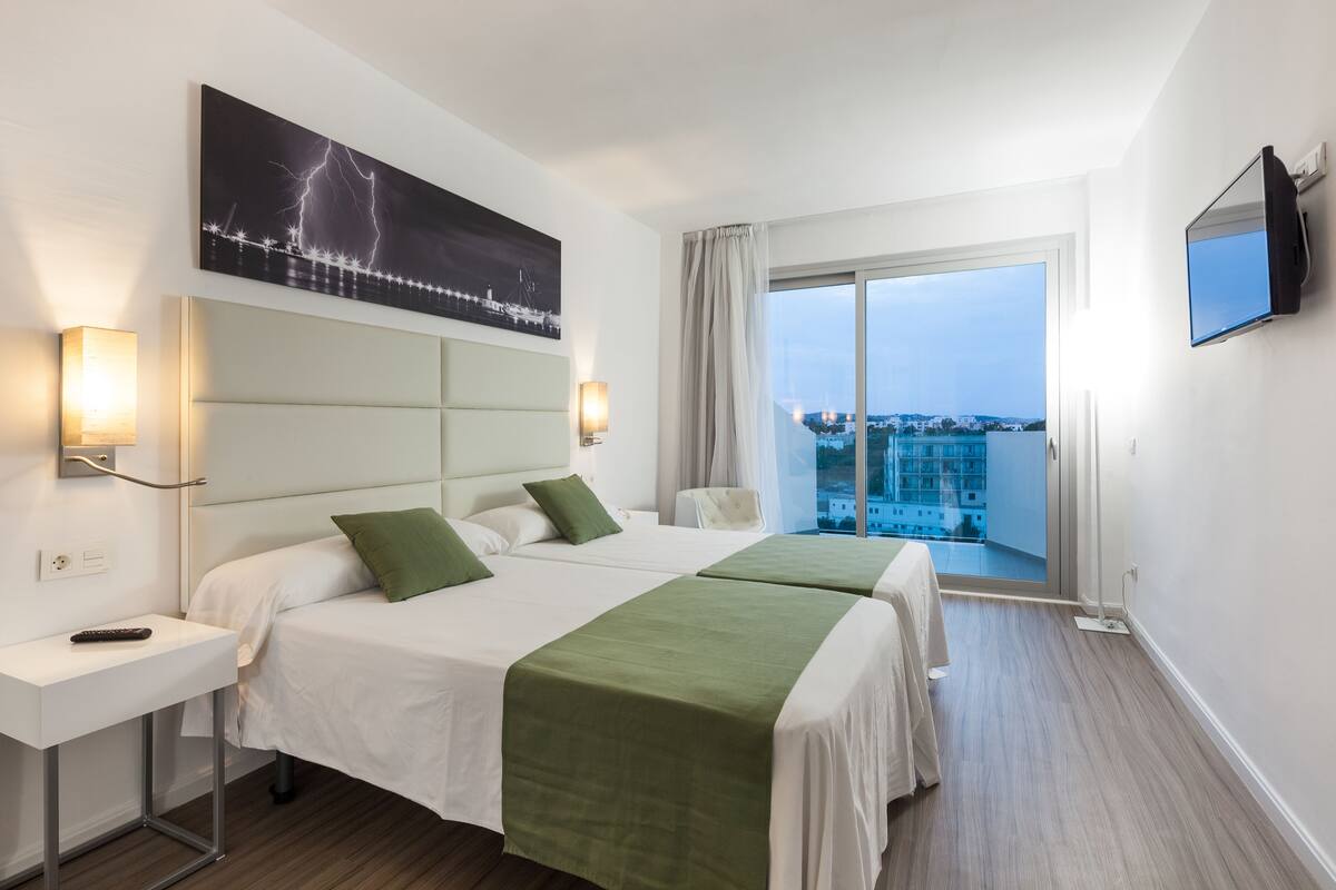 Quarto de hotel com duas camas, uma janela ampla com vista, televisão de tela plana e uma pintura de raios na parede.