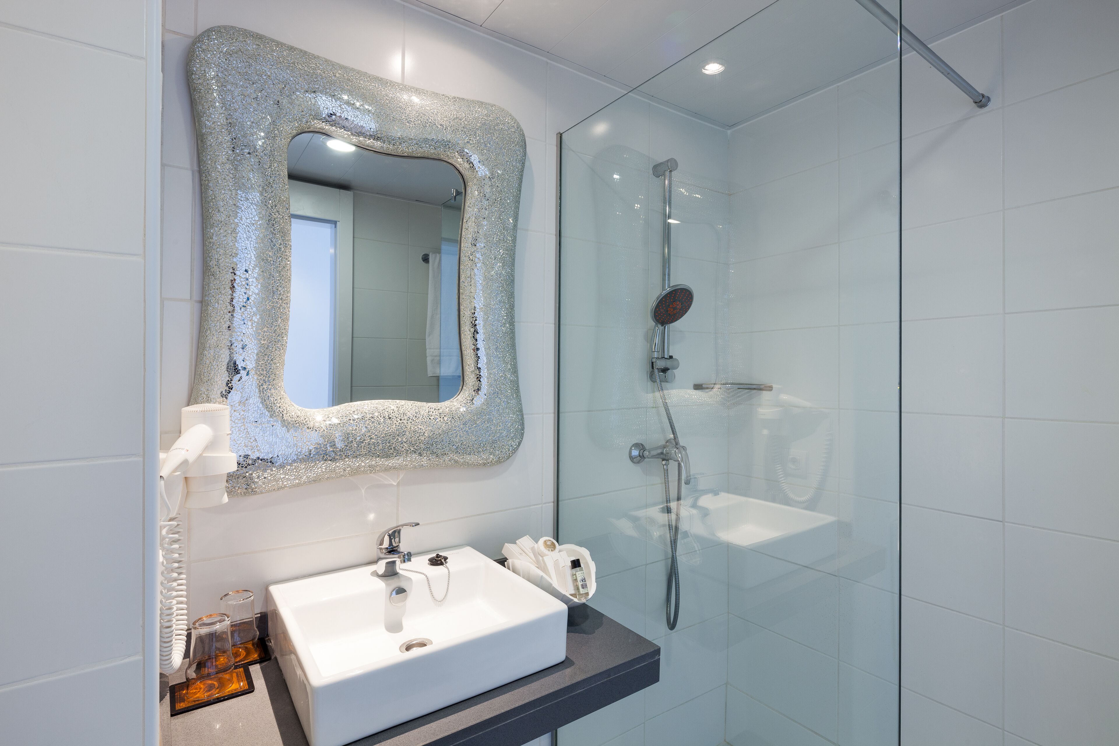 A modern bathroom with a white sink, a large mirror with a textured frame, and a glass-enclosed shower.