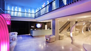 A spacious lobby with a reception desk, seating area, and a staircase leading to an upper level. - Axel Beach Ibiza - Adults Only (Sant Josep de sa Talaia)