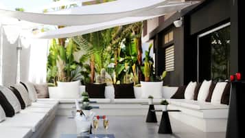 A modern outdoor seating area with white sofas and black cushions, a table with a bottle of champagne, and a glass of wine.