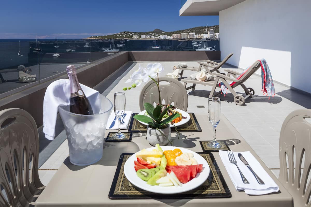 Varanda com mesa posta para dois, com prato de frutas, garrafa de champanhe e vista para o porto de iates.