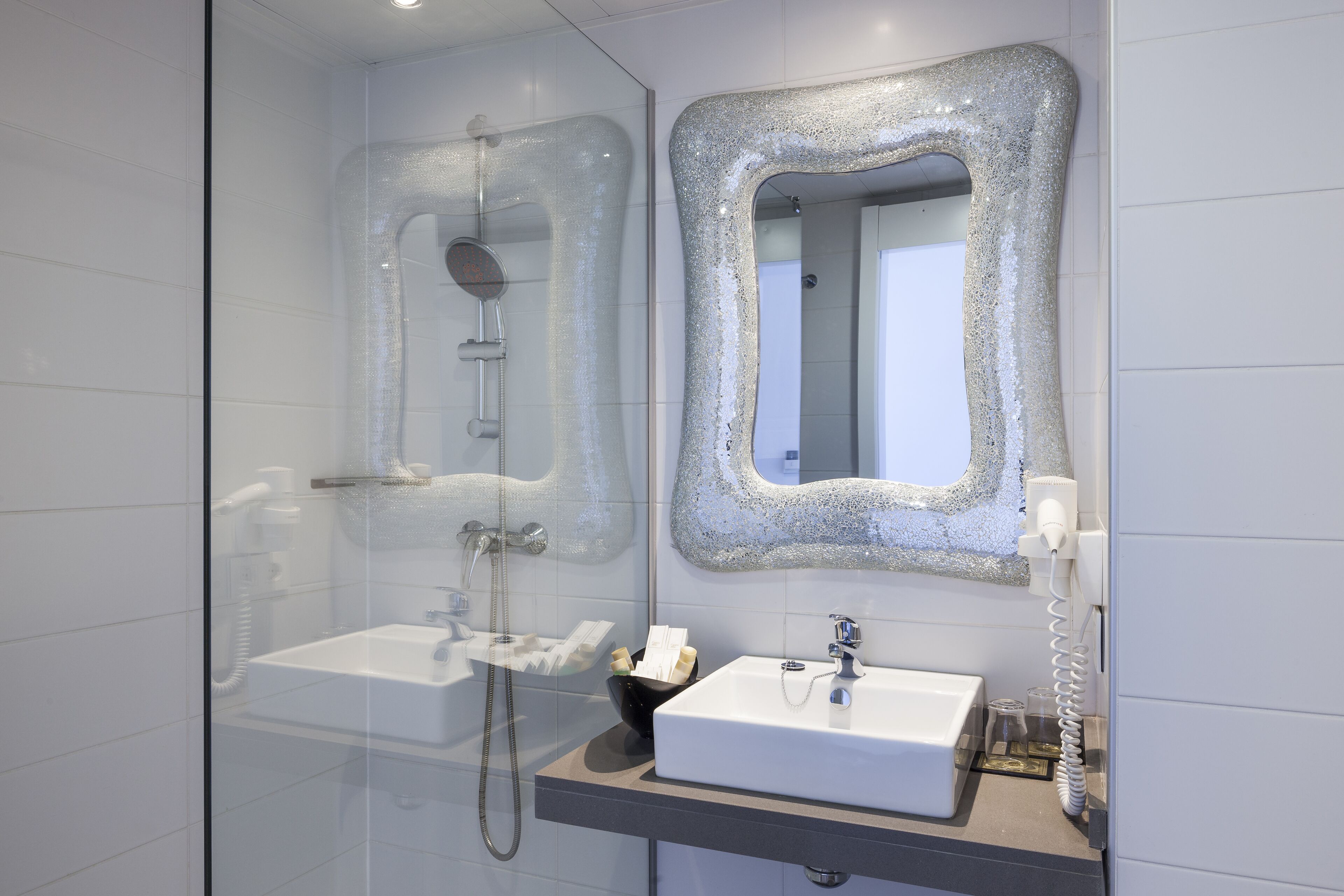 Bany modern amb dutxa de vidre, un lavabo blanc i un mirall amb marc texturat.