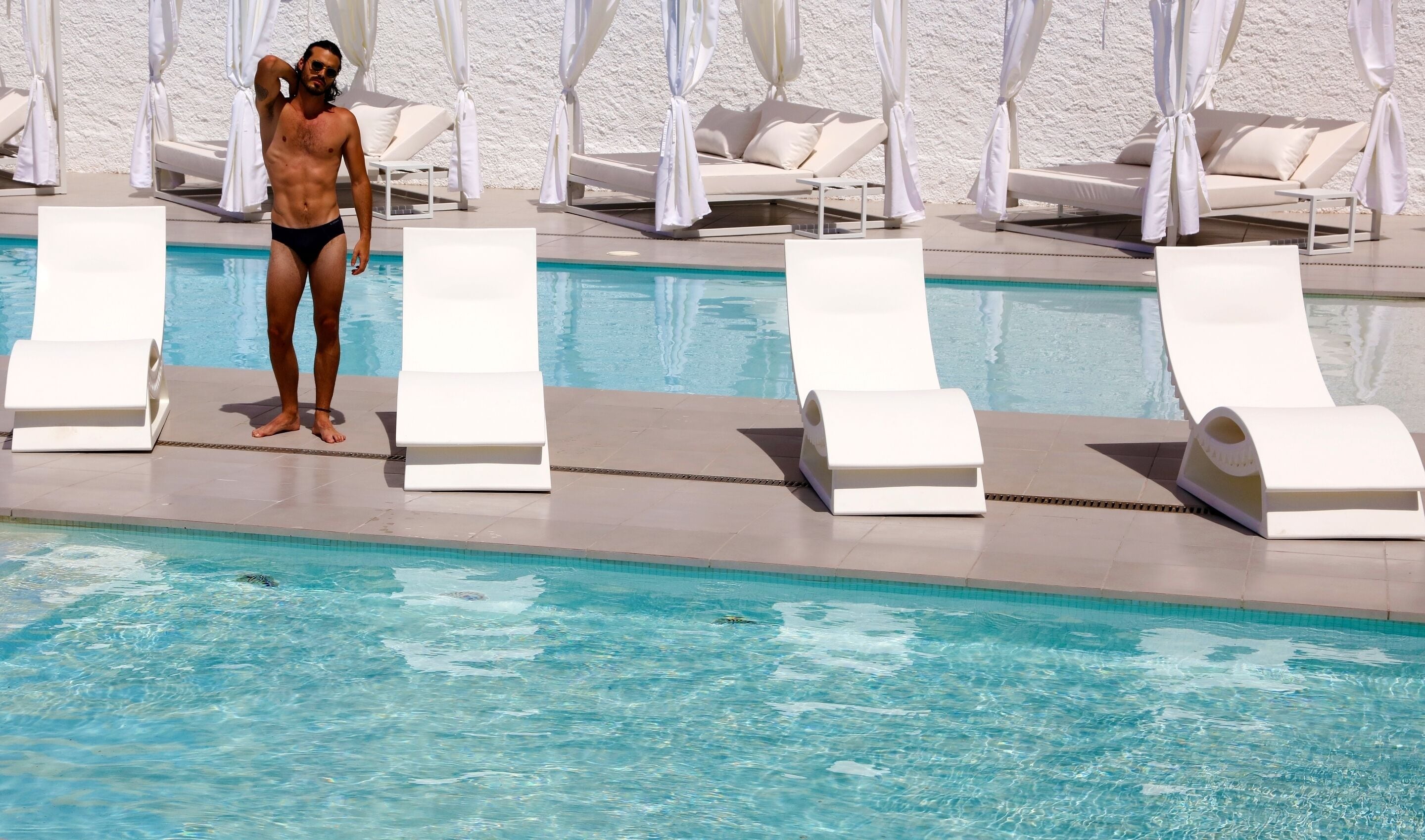A poolside area with lounge chairs and a person standing by the pool.