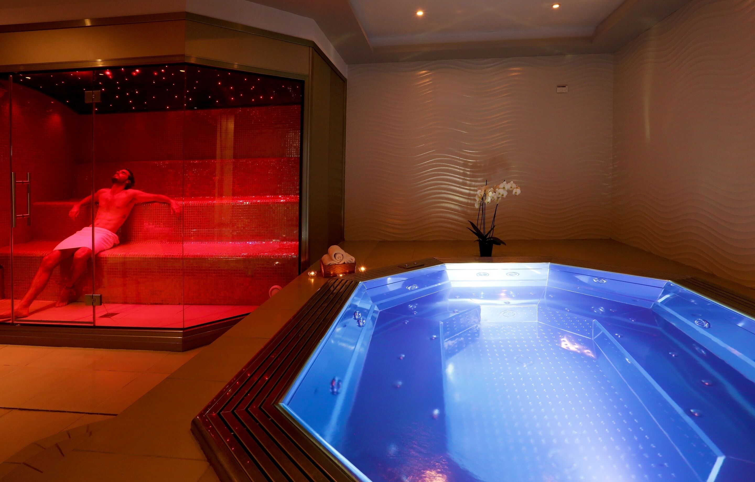 A spa area with a glass-enclosed hot tub and a separate room with a red-lit massage chair.