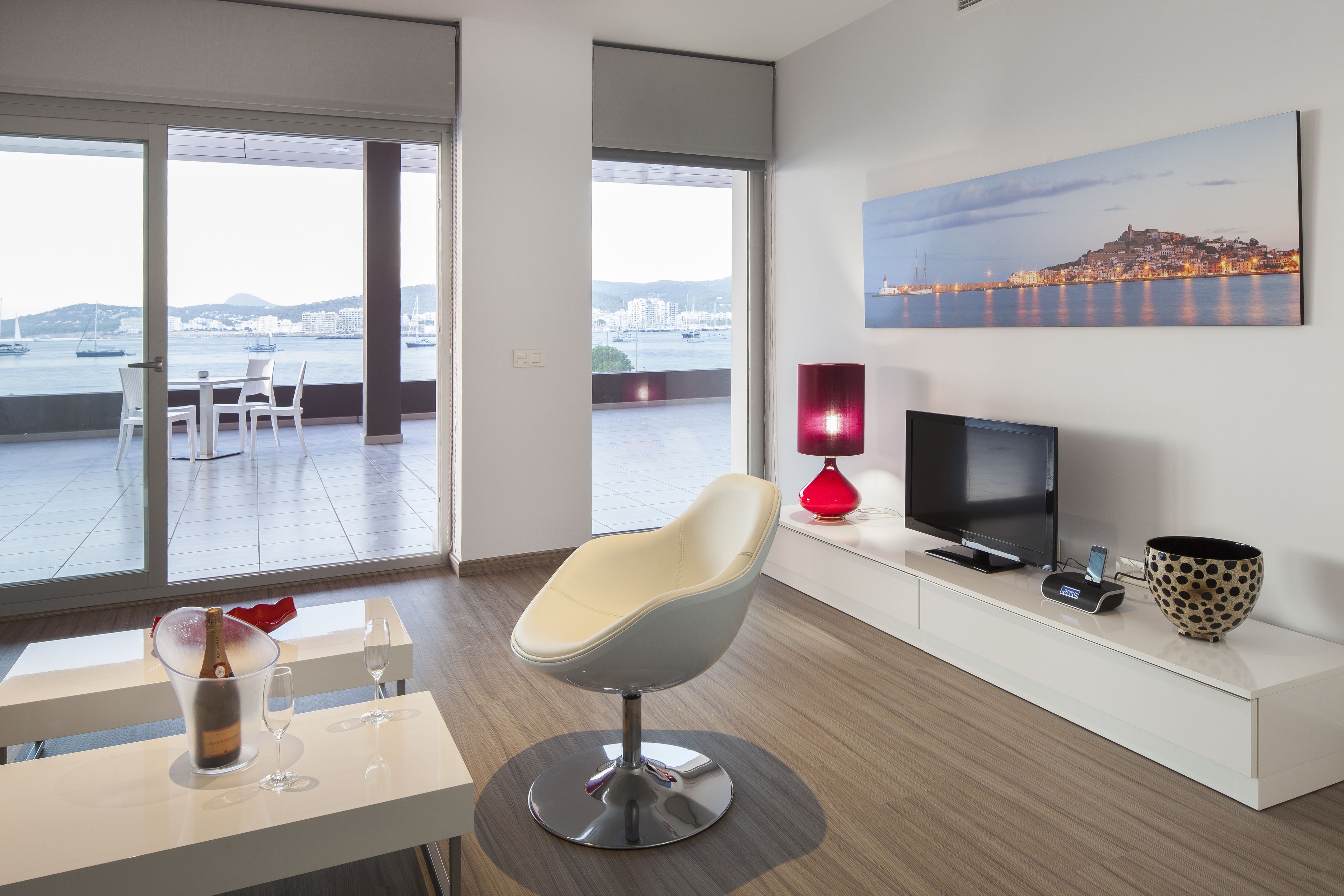 A modern living room with a large window, a TV, a red lamp, and a wine glass on a table.