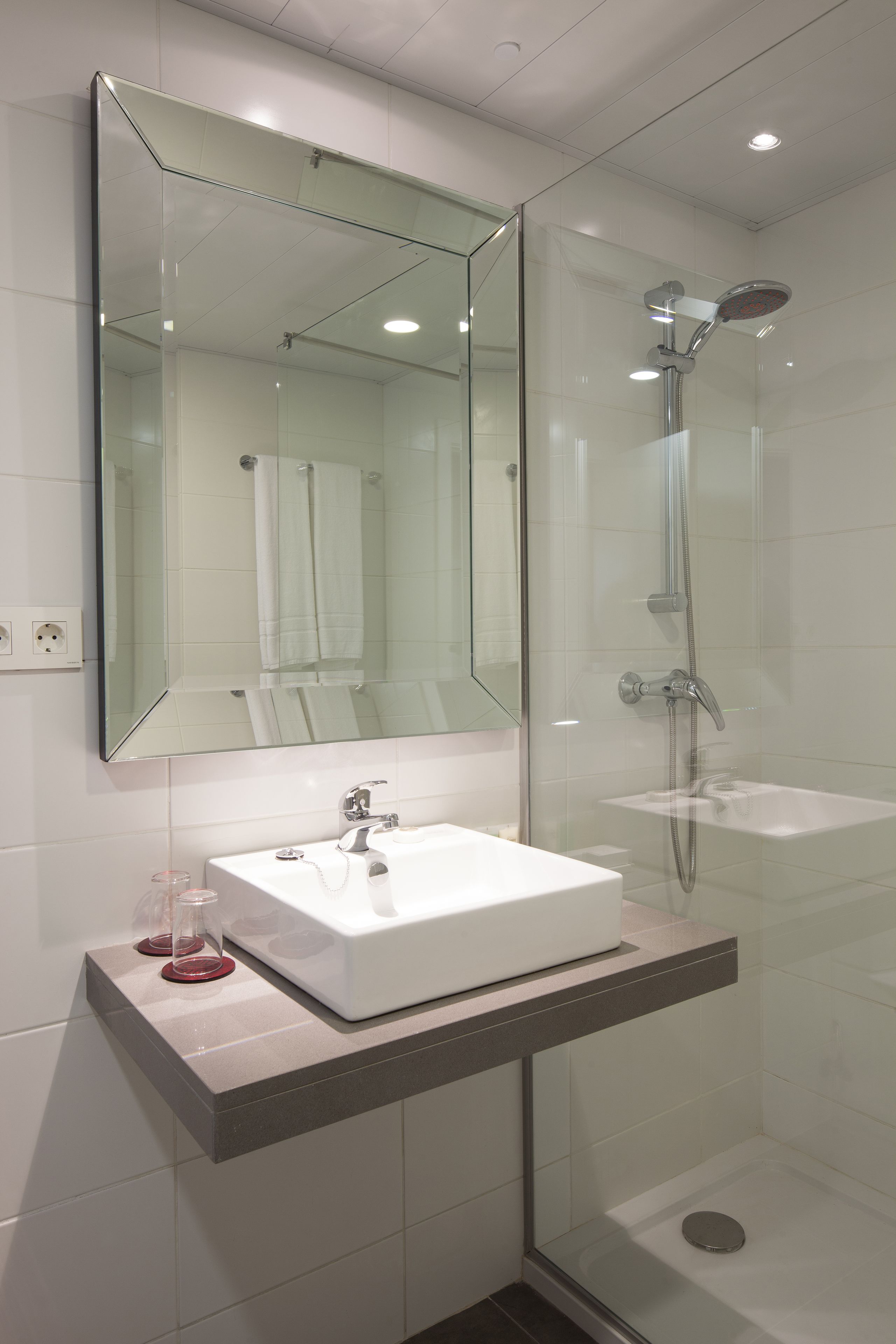 A modern bathroom with a glass-enclosed shower, a white sink, and a large mirror.