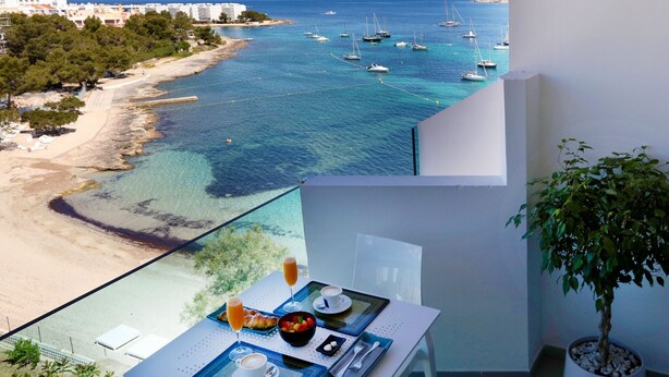 A balcony with a table set for breakfast overlooking a coastal area with boats and a beach. - Axel Beach Ibiza - Adults Only (Sant Josep de sa Talaia)