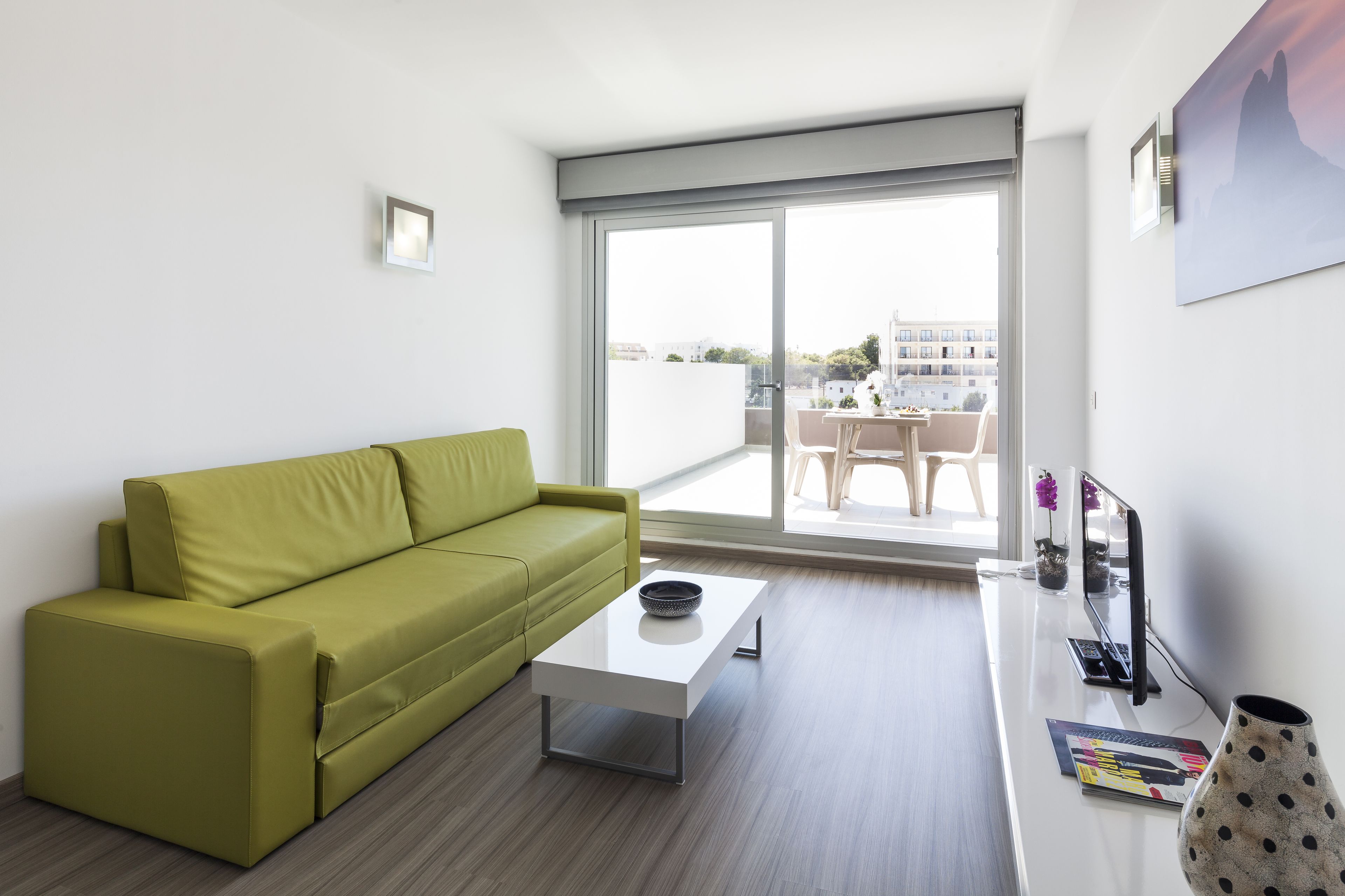 Una sala de estar moderna con un sofá verde, una mesa de centro blanca y un ventanal con vistas a la ciudad.