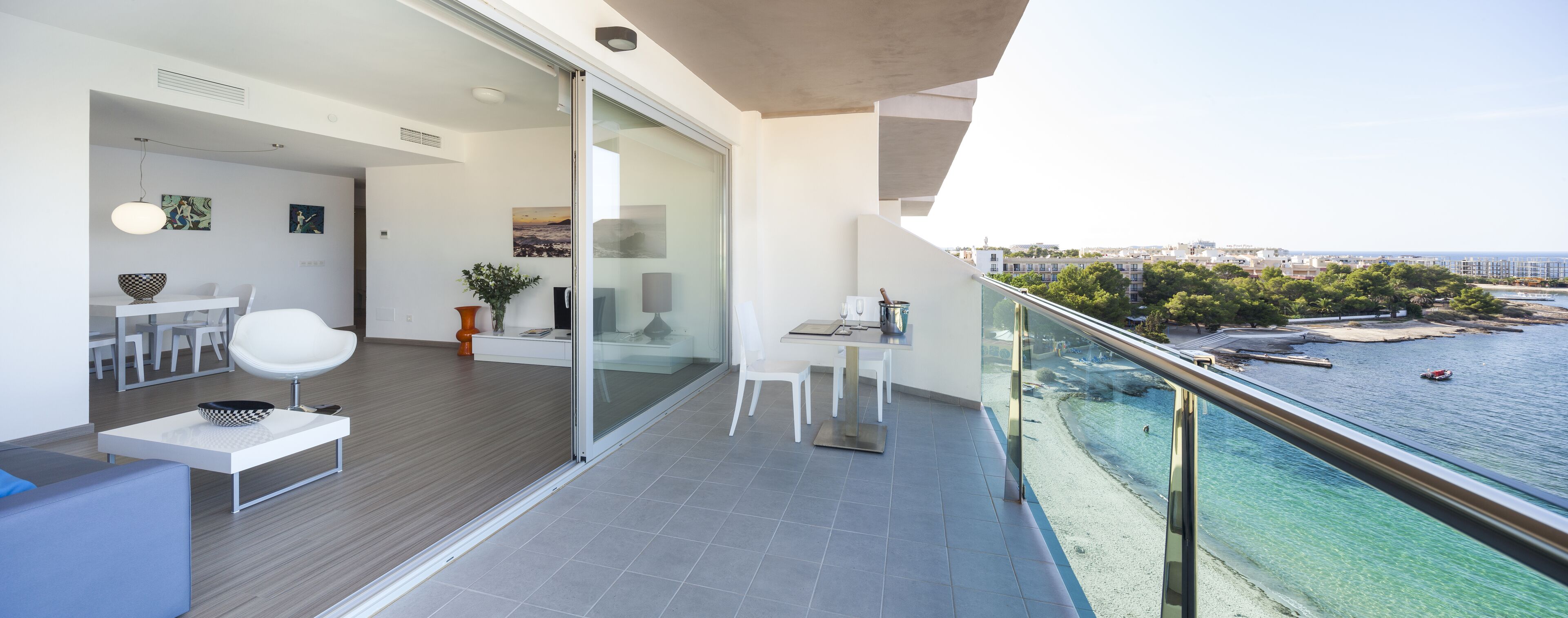 Un balcón moderno con barandilla de vidrio que da a una playa y al horizonte urbano.