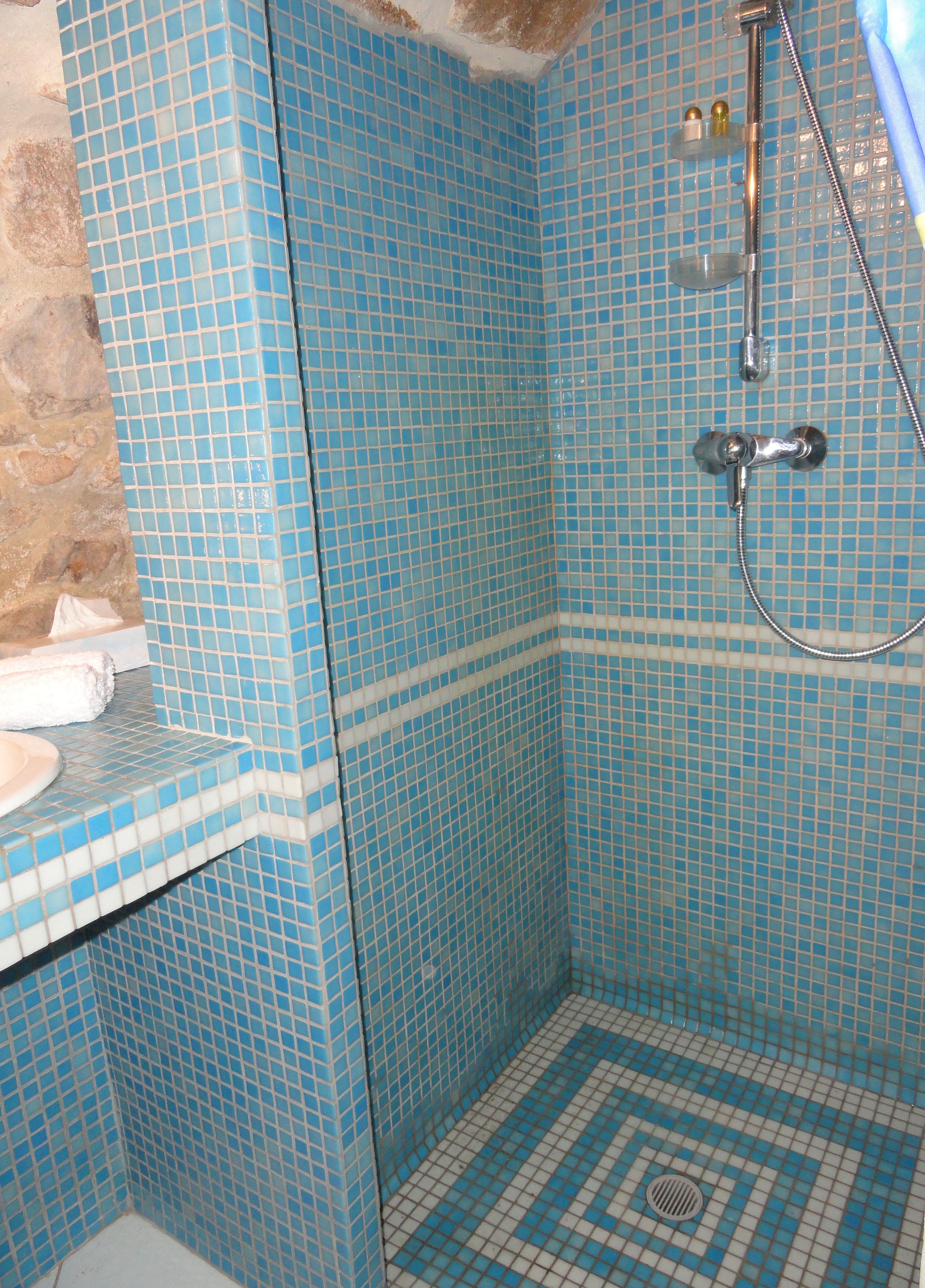 Ein Badezimmer mit blauen Mosaikfliesen, einer Dusche und einem Waschbecken mit Handtuch.