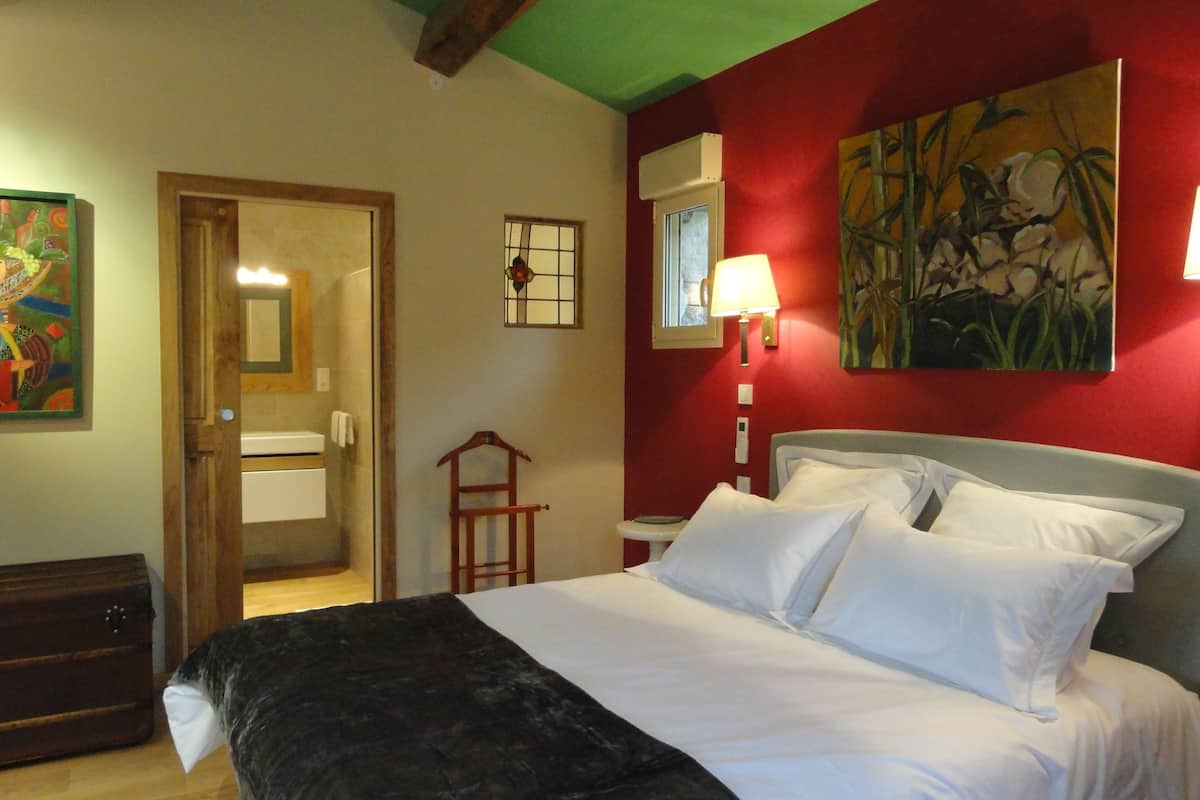 A hotel room with a bed, a bedside lamp, a painting, and a wooden chair.