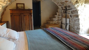 Une chambre avec un plafond en pierre, un lit recouvert d’une couverture à rayures, une commode en bois et un porte-manteau.